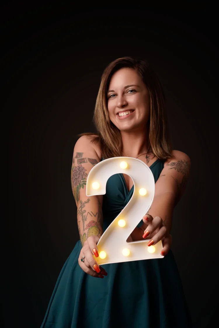 Stephanie Bosworth smiling and holding a lit white number 2 marquee sign, celebrating two years of Emerald Photography
